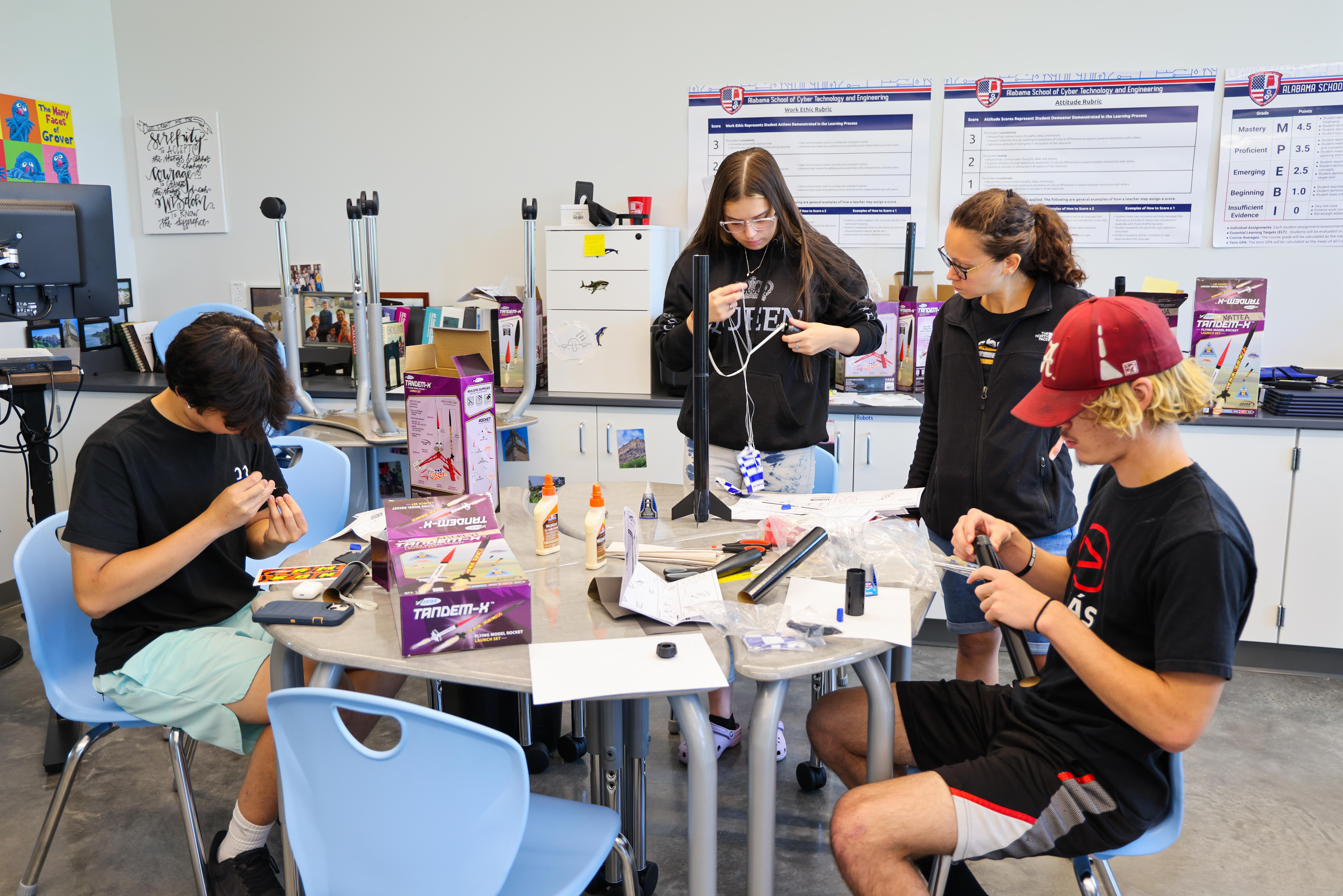 Students sitting and standing around a table working on rockets.