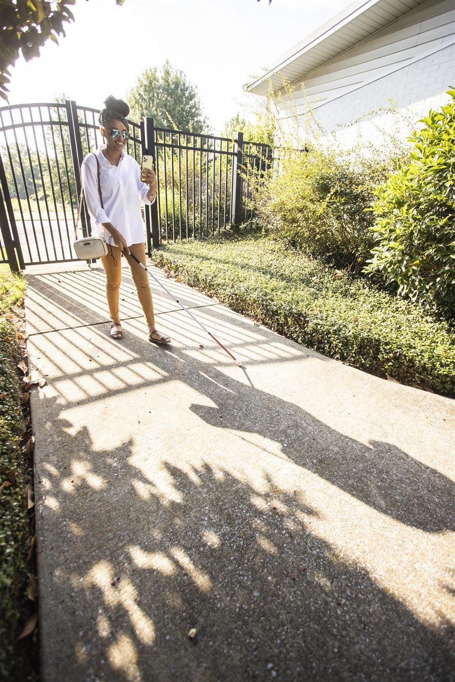  Jonesti Steele walks down a sidewalk between buildings using a phone and white cane to navigate. 