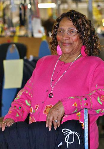 Rushie Cochran sits smiling in a chair with the AIB production floor in the background. 