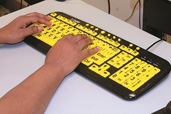 A closeup of two hands typing on a keyboard with large-sized keys for DeafBlind clients at EGH 