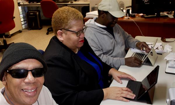 Two adult clients who are blind working with the teacher on mobile devices