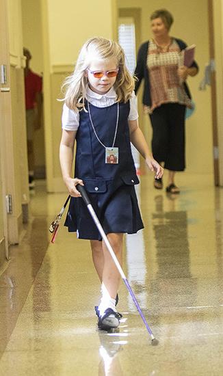 Photo of young girl walking the hall at ASB using her cane. 