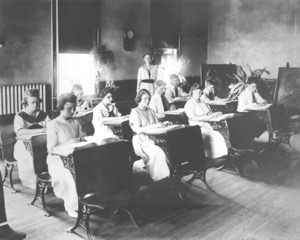 A teacher instructs female students in a turn-of-the-century classroom 