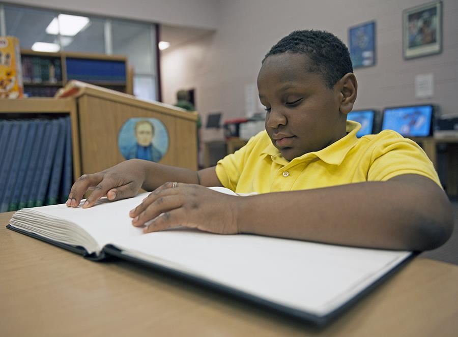 An ASB student uses braille to read a book in the library