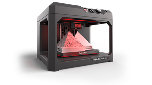 Picture of the Makerbot Replicator Plus printer.  Black frame with red light shining on an object that has just been printed 