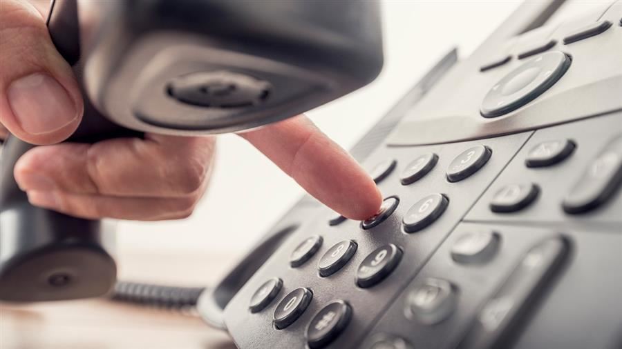 a landline phone with hand holding receiver dialing.