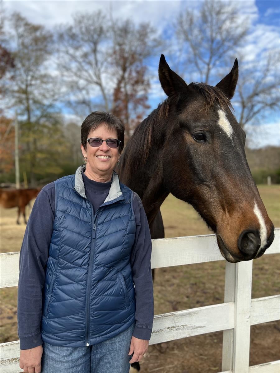Michele smiles to camera while standing beside a horse.