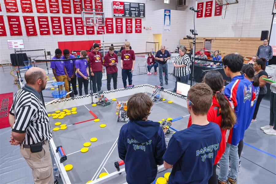 A robotics field with teams on either side and two referees. 