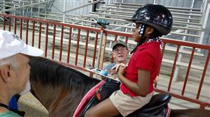 student on horseback interacting with a side walker and a clipboard with small pictures on it 