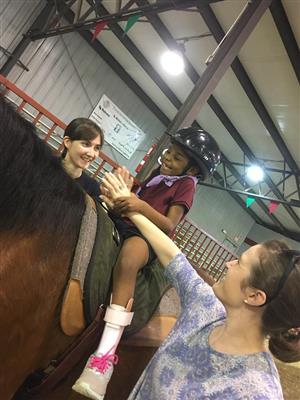 young student riding brown horse and clapping with the hands of two side walkers  