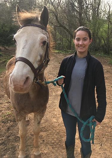 MGHSE student worker Anna stands beside a horse 