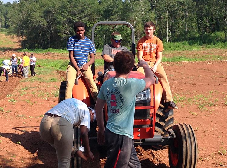 Several students and teacher are on a tractor plowing a feild. Several students and teacher are on a tractor plowing a feild.