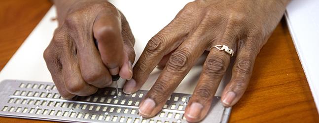 Closeup photo of the hands of a client writing in braille 