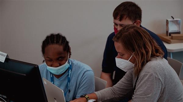 Close up of mentor seated next to a student aiding him with his computer