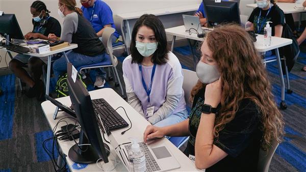 A GenCyber student and mentor are sitting at a computer while working on assignments.