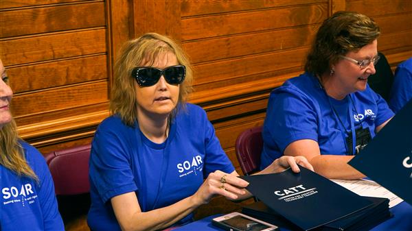 Seated behind a table, CATT faculty hand out blue CATT folders