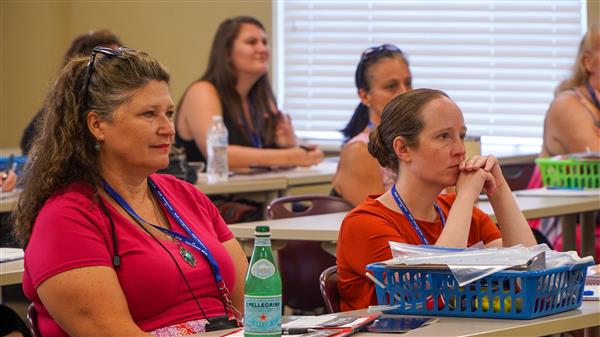 Two women in the foreground, seated, are listening to a presentation.