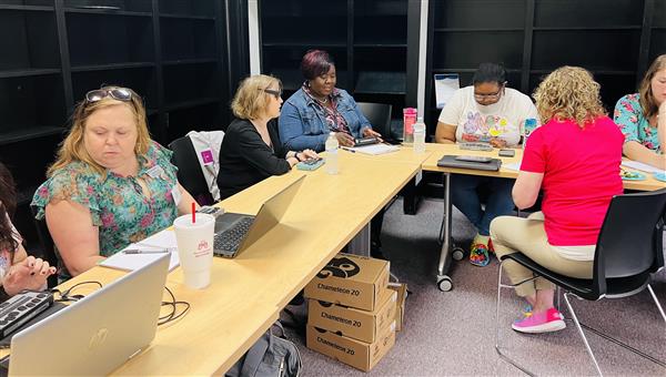Trainer Jill Dunaway sits at a large L shaped desk with a student and teachers