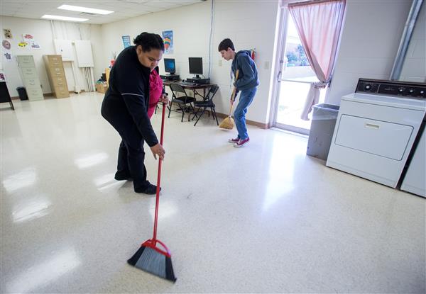Two students sweep the classroom with a broom.